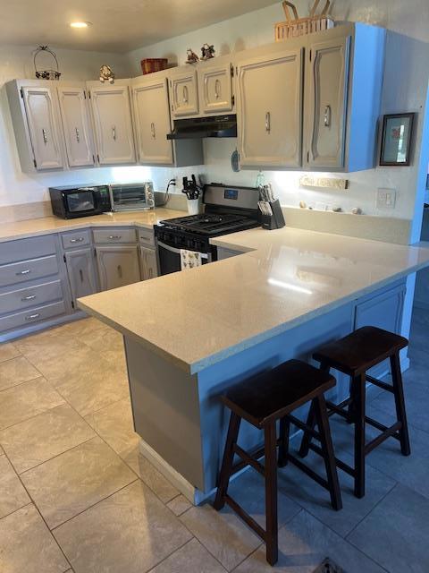 kitchen with stainless steel gas stove, a kitchen breakfast bar, kitchen peninsula, light tile patterned floors, and gray cabinetry