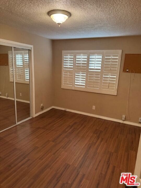 unfurnished bedroom featuring dark hardwood / wood-style floors, a textured ceiling, and a closet