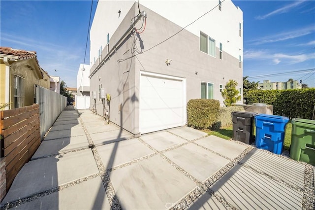 view of side of property with a garage, fence, concrete driveway, and stucco siding