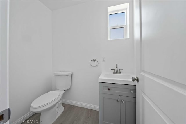 half bathroom featuring toilet, baseboards, wood finished floors, and vanity