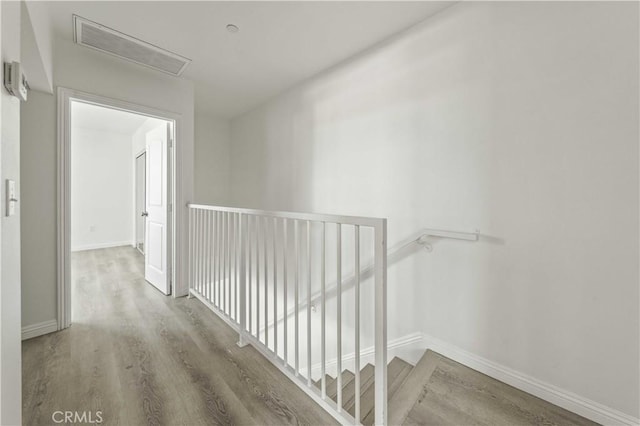 corridor featuring wood finished floors, an upstairs landing, and baseboards