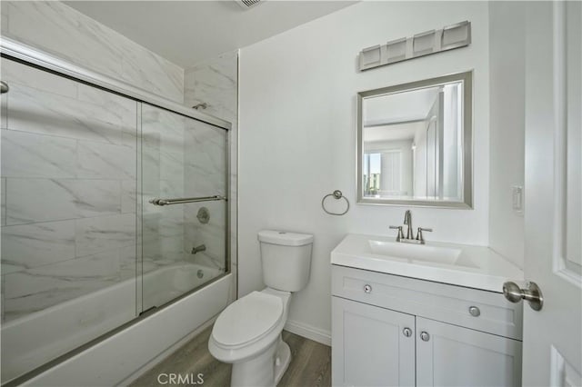 bathroom with bath / shower combo with glass door, toilet, vanity, wood finished floors, and baseboards