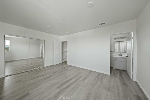 unfurnished bedroom with ensuite bathroom, light hardwood / wood-style floors, sink, and a closet