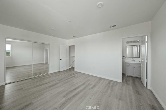 unfurnished bedroom with visible vents, baseboards, a sink, light wood-style floors, and a closet