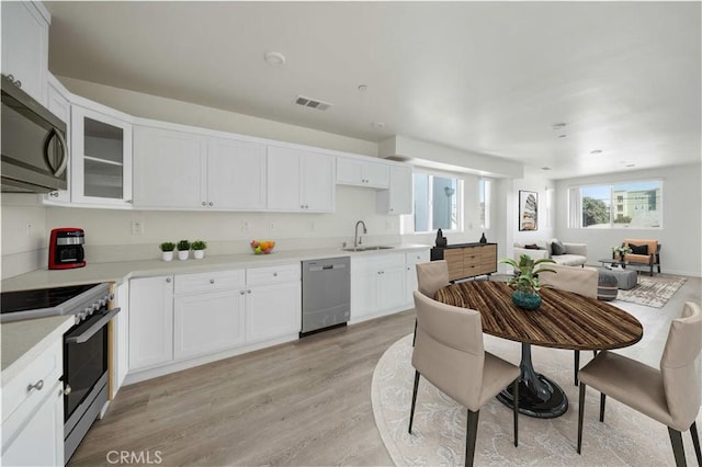 kitchen with light wood finished floors, stainless steel appliances, visible vents, white cabinets, and a sink