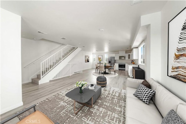 living room featuring baseboards, stairway, visible vents, and light wood-style floors