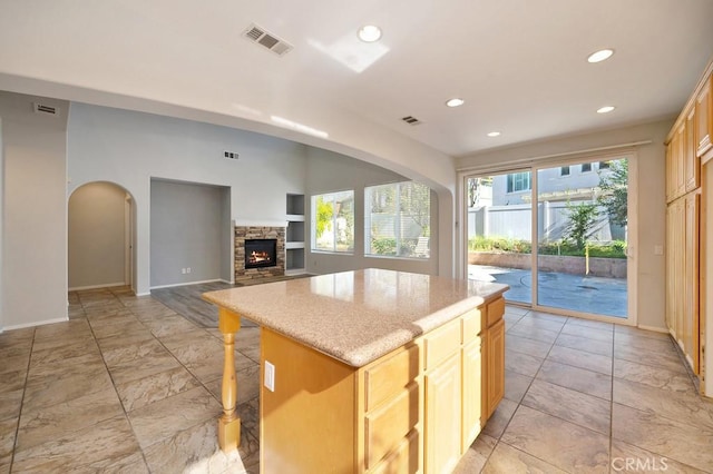 kitchen featuring a fireplace, light brown cabinets, a kitchen island, and a breakfast bar area