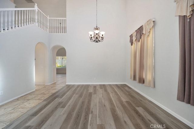 empty room featuring light hardwood / wood-style flooring, a high ceiling, and a notable chandelier