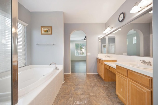 bathroom featuring plenty of natural light, ceiling fan, vanity, and tiled tub