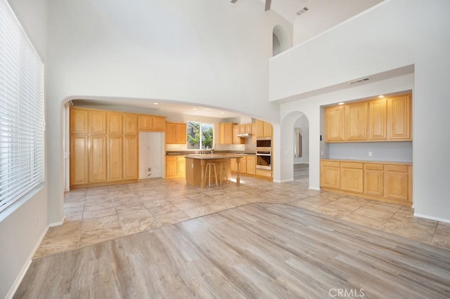 kitchen with stainless steel microwave, a high ceiling, light hardwood / wood-style flooring, light brown cabinetry, and a kitchen island