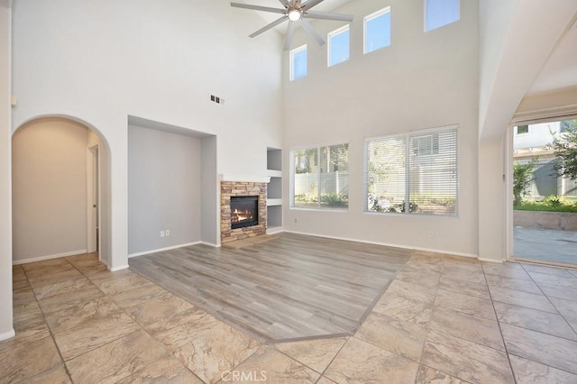 unfurnished living room featuring a fireplace, a high ceiling, built in features, and ceiling fan