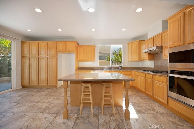 kitchen featuring a breakfast bar, light stone countertops, stainless steel appliances, light brown cabinetry, and a kitchen island