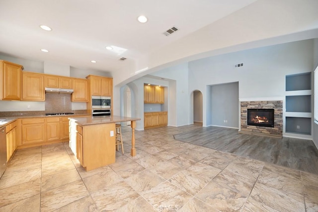 kitchen with light brown cabinetry, a breakfast bar, stainless steel appliances, built in features, and a center island