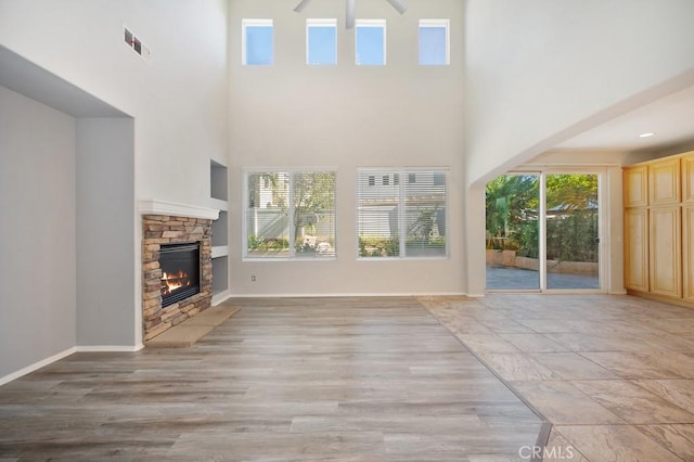 unfurnished living room featuring a high ceiling, light hardwood / wood-style floors, and a stone fireplace