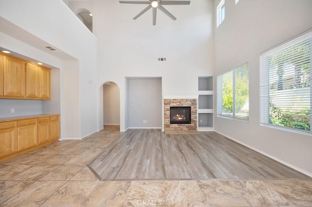 unfurnished living room featuring a towering ceiling, ceiling fan, light hardwood / wood-style flooring, built in features, and a fireplace