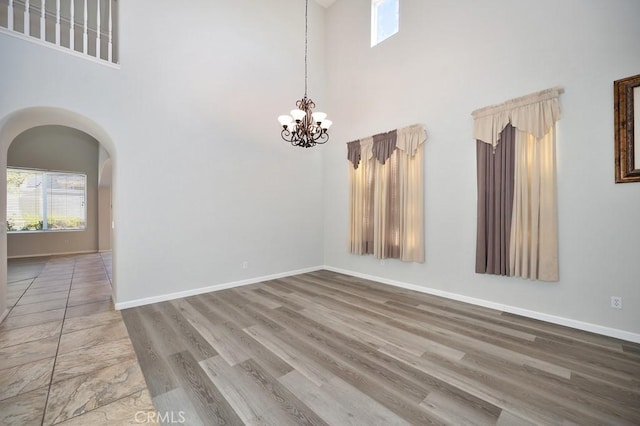 empty room featuring hardwood / wood-style floors, a towering ceiling, and an inviting chandelier