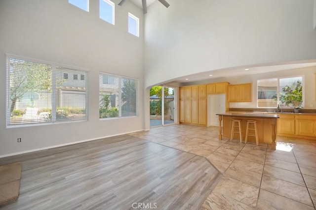 unfurnished living room with light wood-type flooring, a towering ceiling, plenty of natural light, and ceiling fan