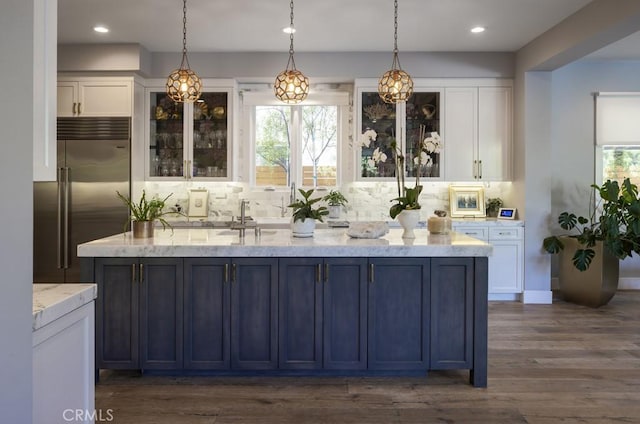 bar with tasteful backsplash, white cabinetry, built in refrigerator, pendant lighting, and light stone counters