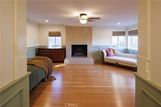 bedroom featuring a large fireplace, light hardwood / wood-style floors, multiple windows, and ceiling fan