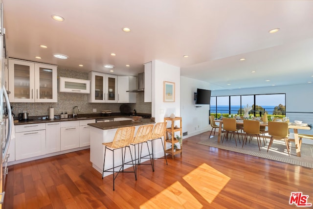 kitchen with decorative backsplash, white cabinetry, hardwood / wood-style floors, and wall chimney exhaust hood