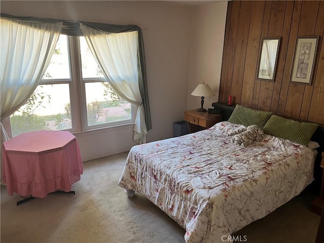 bedroom featuring wooden walls and light carpet