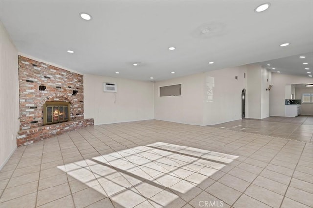 unfurnished living room with light tile patterned floors, vaulted ceiling, a wall mounted AC, and a brick fireplace