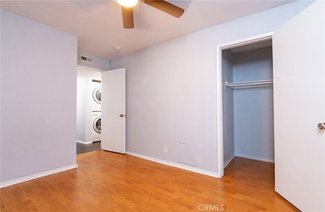 unfurnished bedroom featuring a closet, light hardwood / wood-style floors, ceiling fan, and stacked washer and clothes dryer