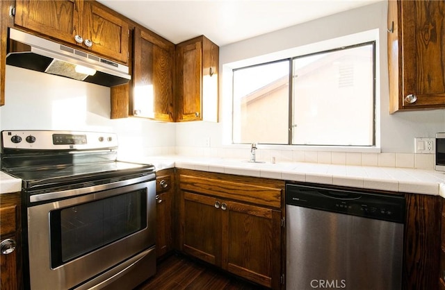 kitchen with tile counters, dark wood-type flooring, and appliances with stainless steel finishes