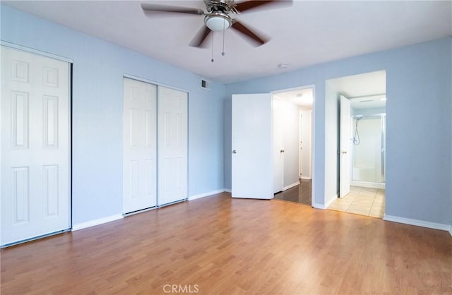 unfurnished bedroom featuring ensuite bath, ceiling fan, light hardwood / wood-style floors, and two closets