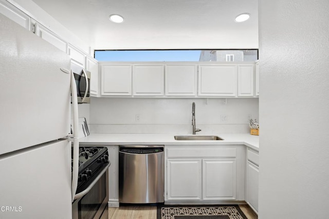 kitchen with light wood-type flooring, stainless steel appliances, white cabinetry, and sink