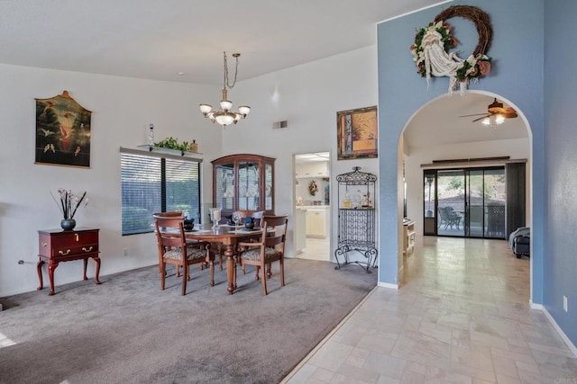 carpeted dining space with ceiling fan with notable chandelier and a towering ceiling