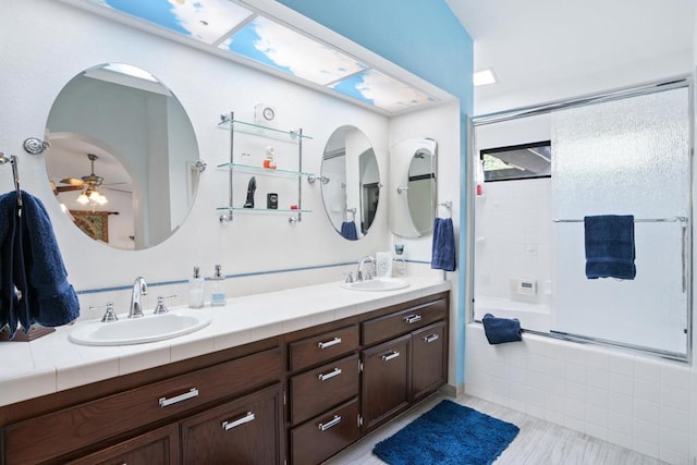 bathroom with a skylight, ceiling fan, vanity, and enclosed tub / shower combo