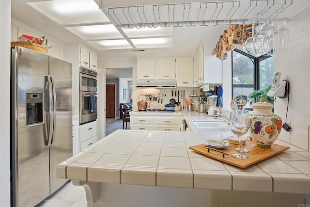 kitchen with sink, kitchen peninsula, tile counters, white cabinetry, and stainless steel appliances