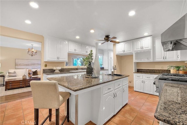 kitchen with a center island, white cabinets, exhaust hood, and ceiling fan with notable chandelier