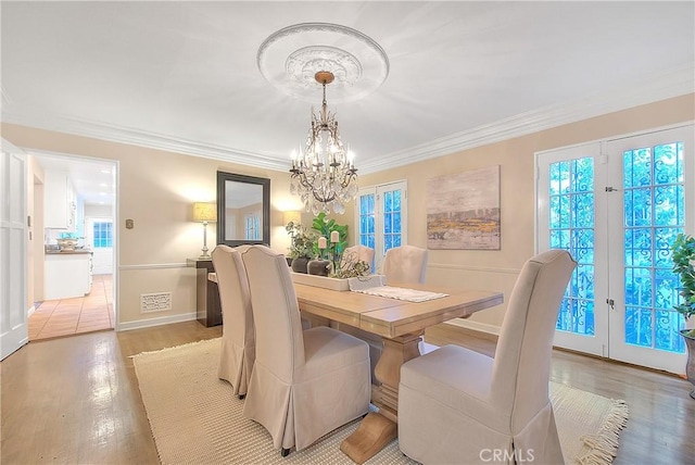 dining room with crown molding, french doors, light hardwood / wood-style floors, and an inviting chandelier