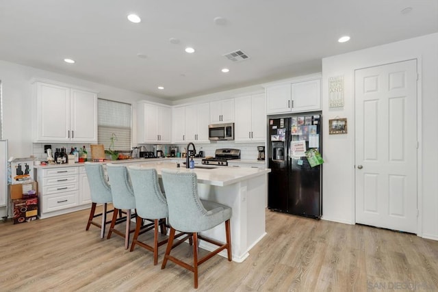 kitchen with white cabinets, appliances with stainless steel finishes, light hardwood / wood-style floors, and an island with sink