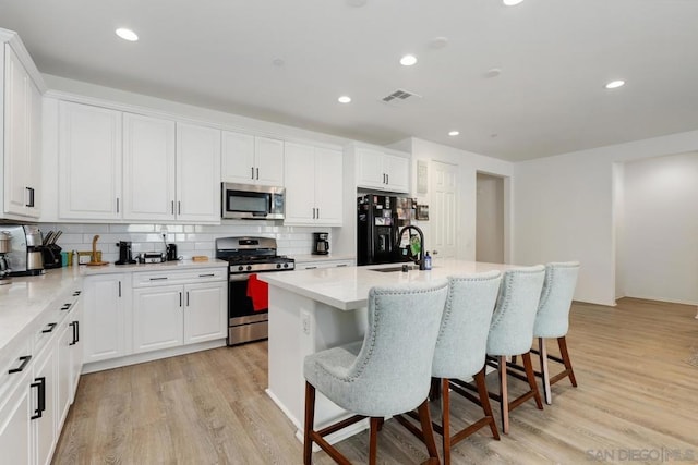 kitchen featuring a breakfast bar, white cabinets, light hardwood / wood-style flooring, an island with sink, and appliances with stainless steel finishes