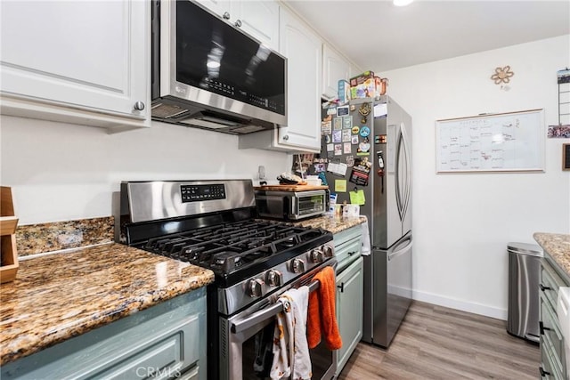 kitchen featuring white cabinets, dark stone countertops, light wood-type flooring, and stainless steel appliances