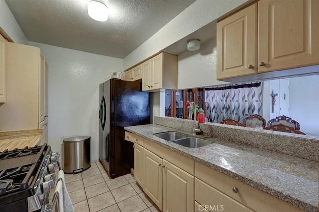 kitchen featuring a textured ceiling, a sink, freestanding refrigerator, light stone countertops, and stainless steel range with gas stovetop