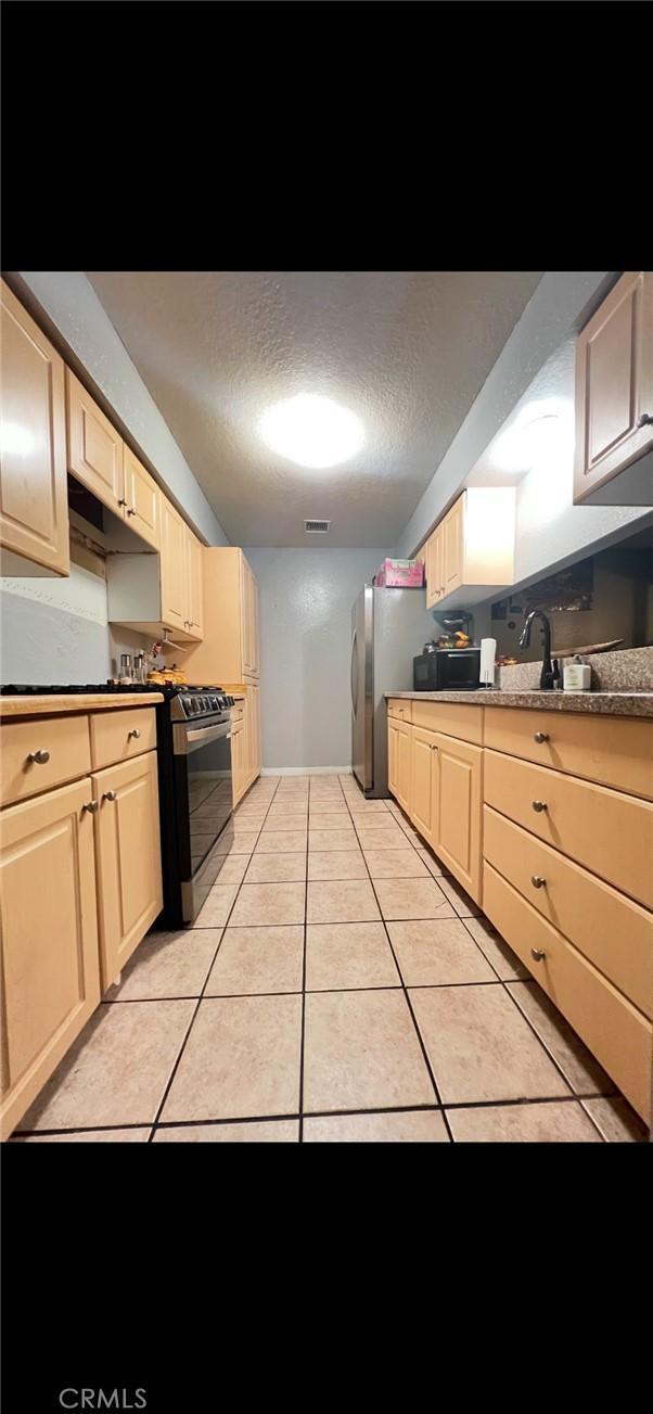 kitchen featuring light tile patterned floors, stainless steel appliances, dark countertops, visible vents, and a textured ceiling