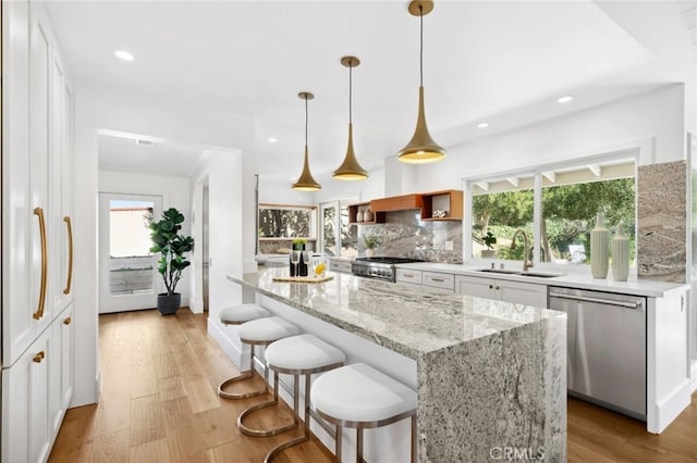 kitchen featuring light wood-type flooring, stainless steel appliances, sink, white cabinetry, and hanging light fixtures