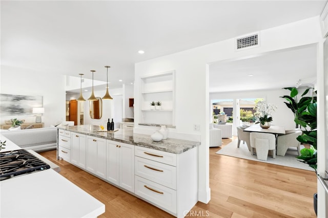 kitchen featuring white cabinets, light hardwood / wood-style floors, light stone counters, and hanging light fixtures