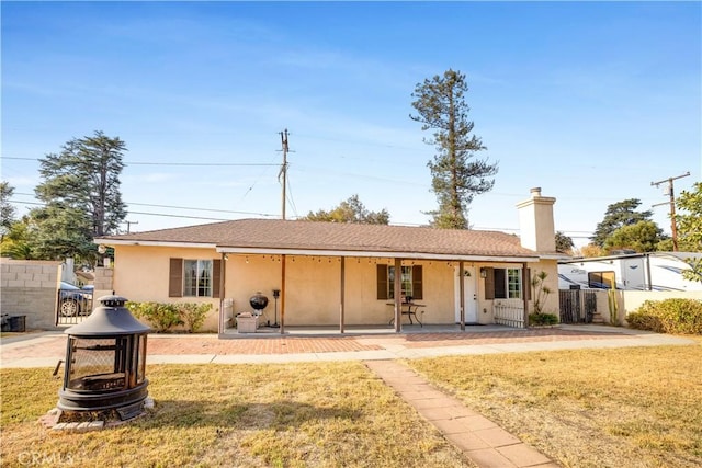 ranch-style house with a porch, a fire pit, and a front yard