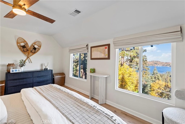 bedroom featuring wood-type flooring, a water view, multiple windows, and lofted ceiling