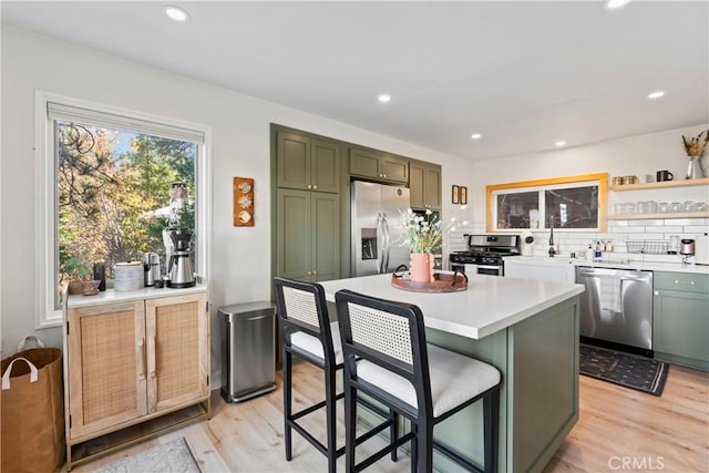 kitchen with a breakfast bar, green cabinets, decorative backsplash, light wood-type flooring, and appliances with stainless steel finishes