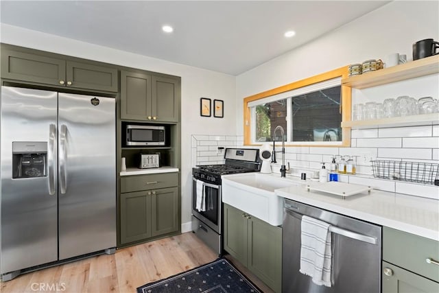 kitchen with tasteful backsplash, green cabinets, stainless steel appliances, and light wood-type flooring