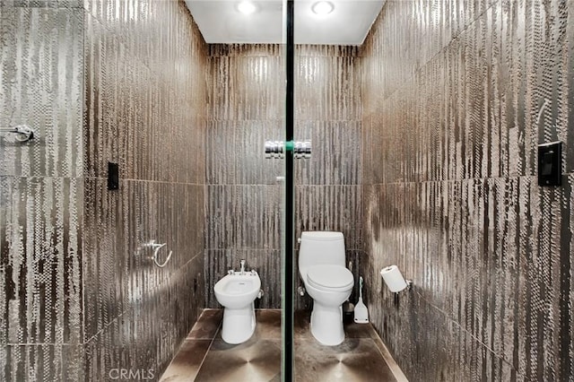 bathroom featuring tile patterned floors, a bidet, toilet, and tile walls