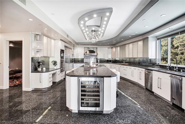 kitchen featuring a center island, a raised ceiling, sink, wine cooler, and white cabinetry