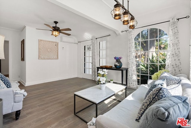 living room featuring ceiling fan with notable chandelier, an AC wall unit, and dark wood-type flooring