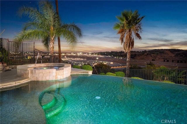 pool at dusk with an in ground hot tub